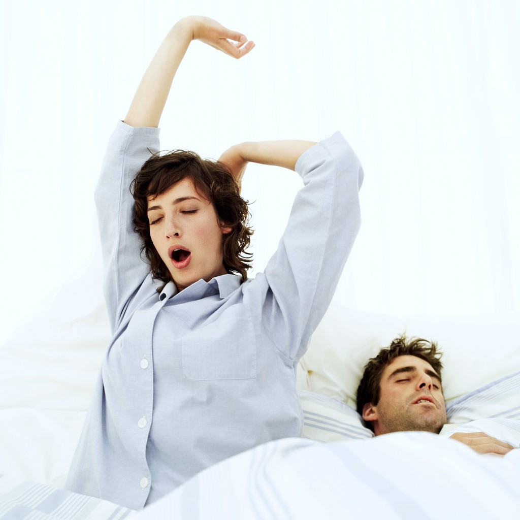 Woman Stretching in Bed with a Man Sleeping Beside Her